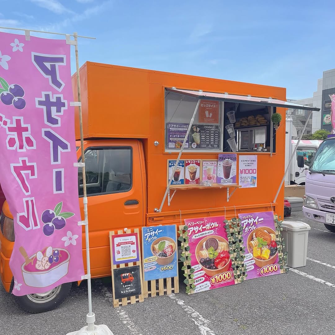 Level up Kitchen のオレンジ色のキッチンカー。アサイーボウルとドリンクのメニューを掲げて出店中の様子